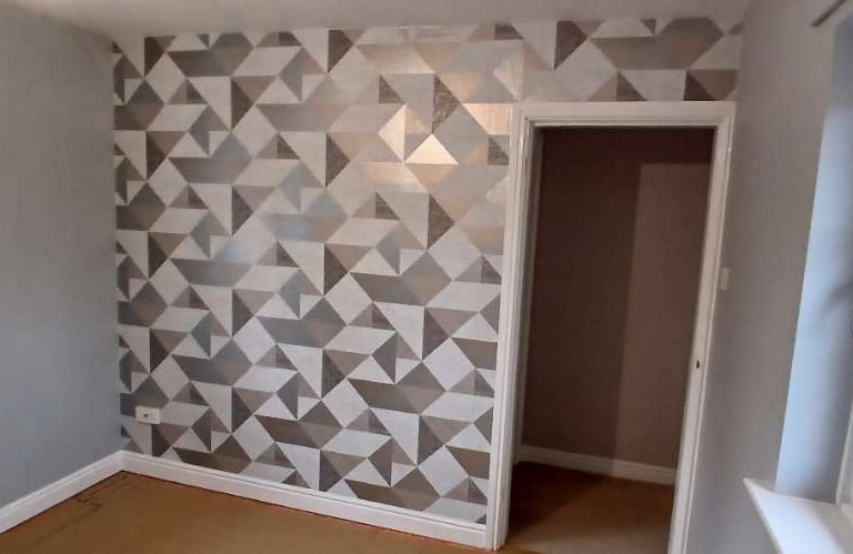 An unfurnished room, with grey walls/ceiling surrounding a triangular/geometric feature wall.