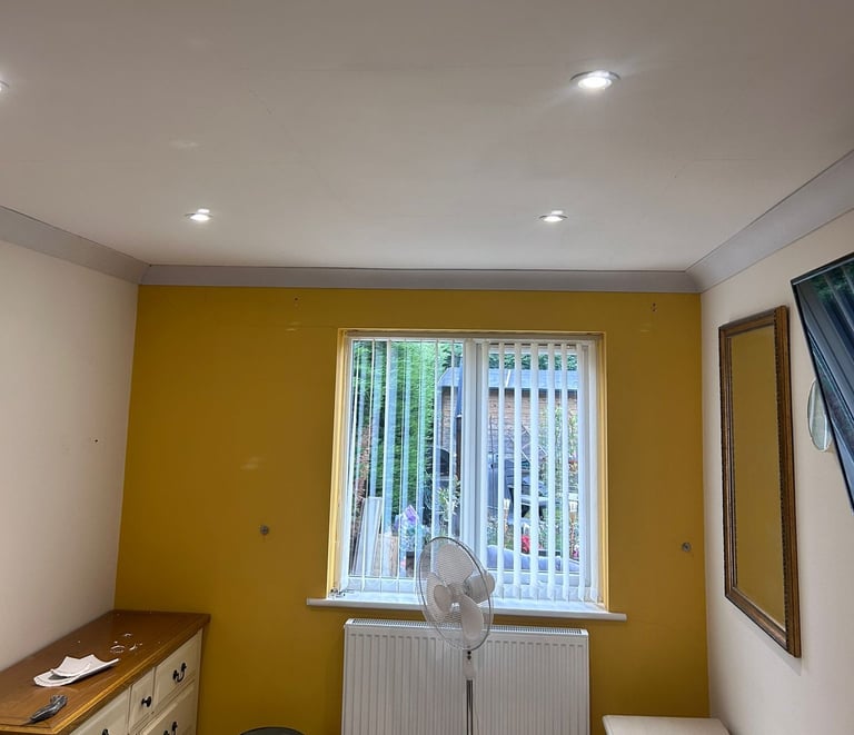 A furnished sitting room, with white ceiling, white walls, and a bright-yellow feature wall.