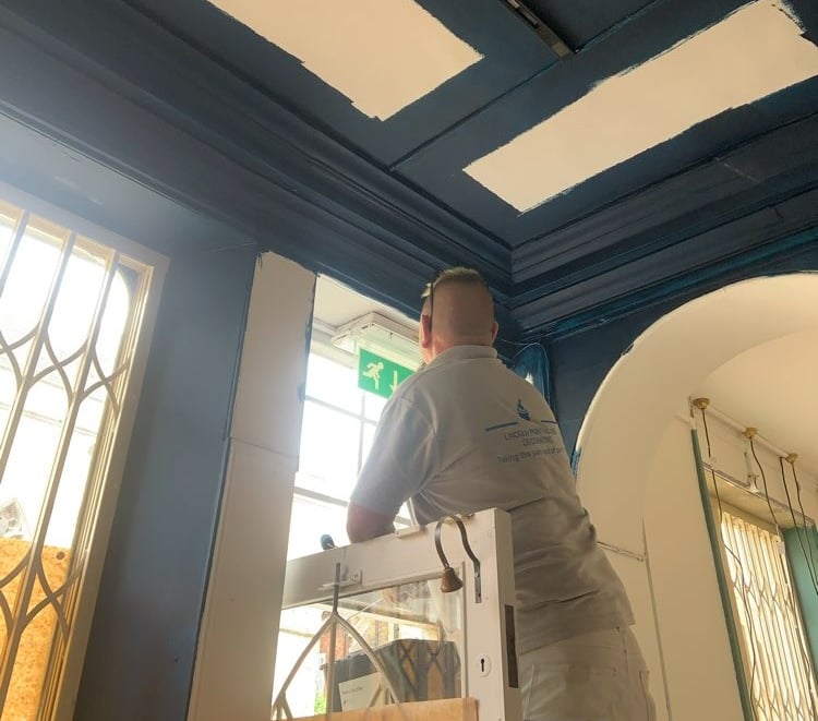 An in-progress navy-blue room, with a painter using a ladder to finish a doorway.