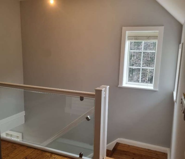 Top of a staircase, with glass banisters, wooden flooring, grey walls, and white detailing.