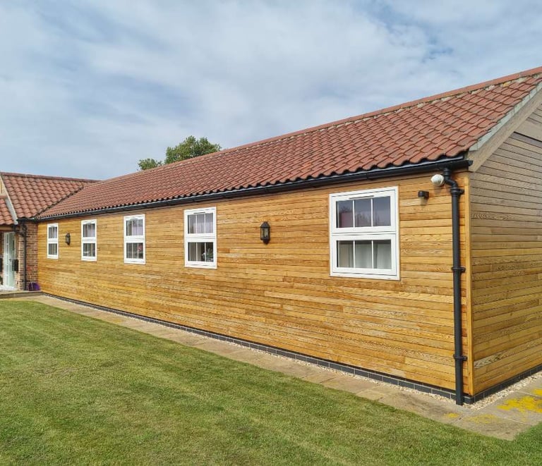 Exterior of long bungalow, with wood panelling on all walls, white windows, and maroon roof tiles.