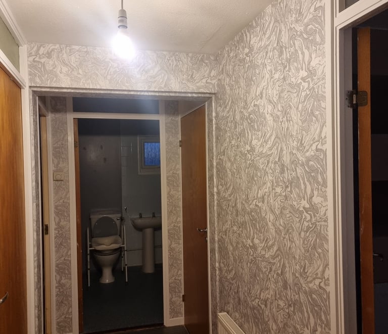 A hallway with 5 wooden doors, alongside marble-like wallpaper on all walls.