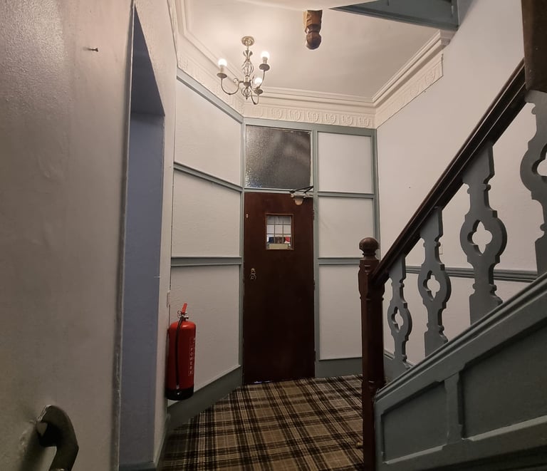 Bottom of a stairway leading to a door, with grey walls and green/dark-grey detailing and banister.