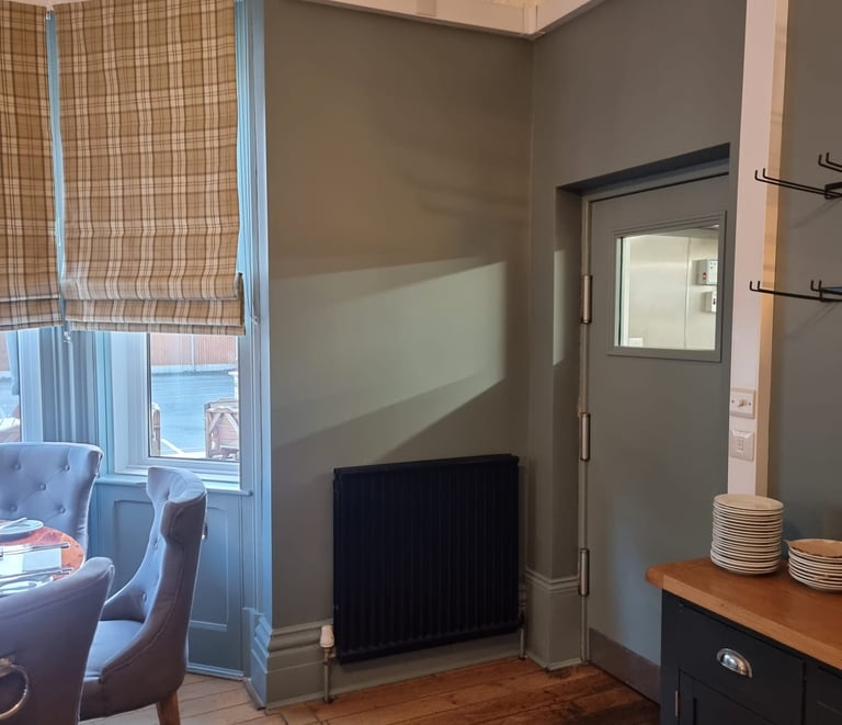 Corner of restaurant dining room, with dark-grey door, a window, and black radiator.
