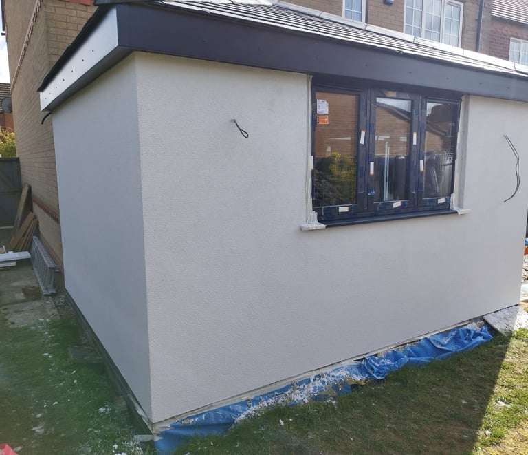Exterior of a small extension being built on a residential home, with walls painted white.