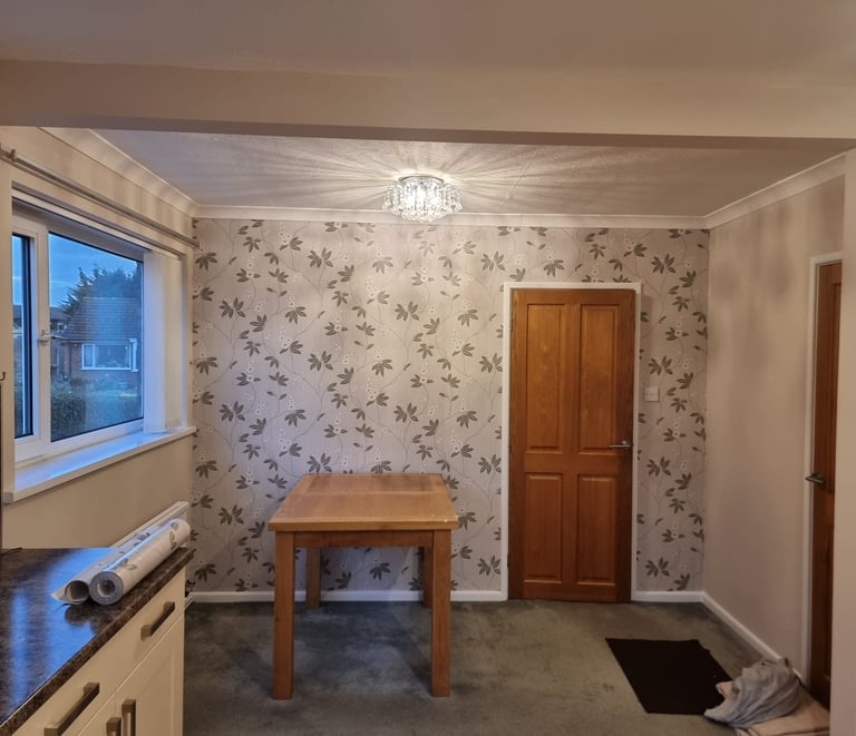 A square dining room, with cream walls, a white ceiling, and a feature wall with a vine-like motif.