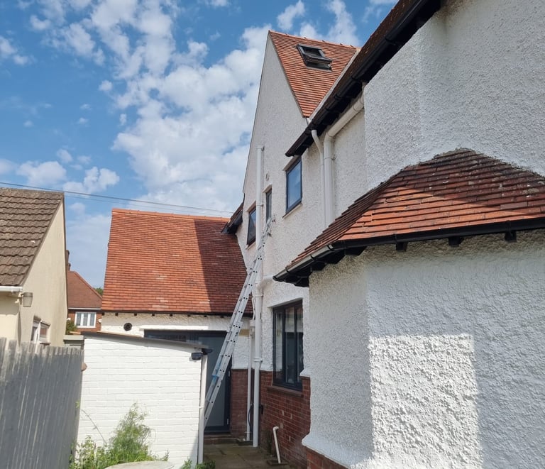 Exterior of the back of a white, stippled residential home, with maroon rooftiles.