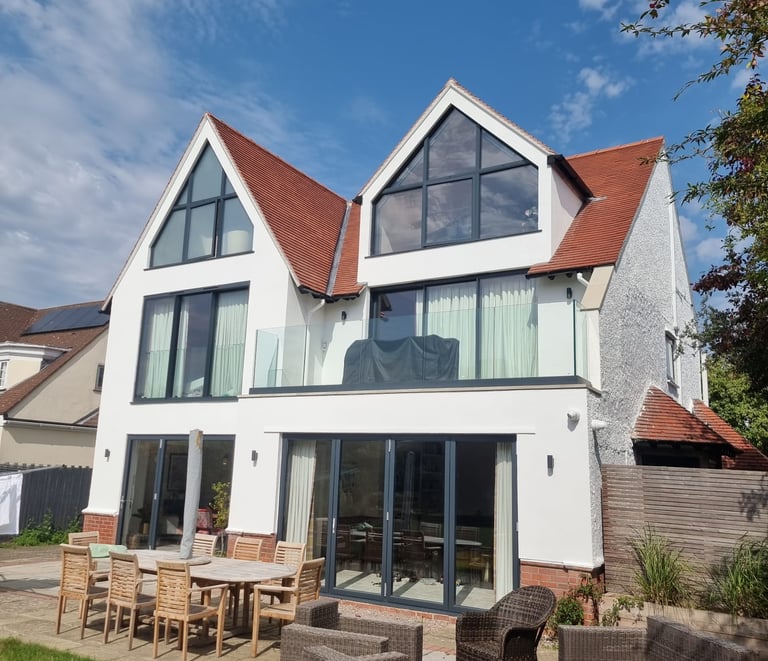 Exterior front of a 3-storey home, that has white-painted walls and many large windows/glass doors.