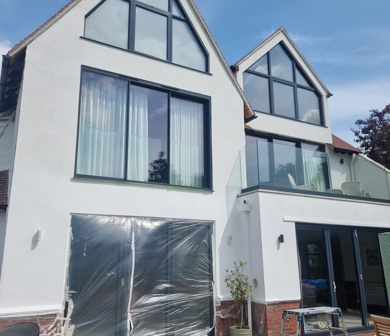 Exterior front of a 3-storey home, that has white-painted walls and many large windows/glass doors.