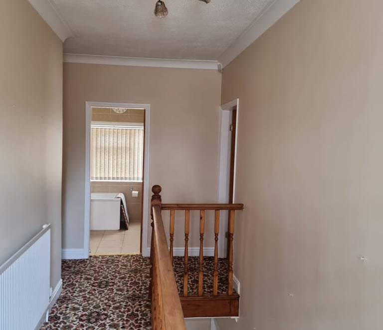 A small upstairs hallway, with painted cream walls, white doorframes, and brown patterned carpet.