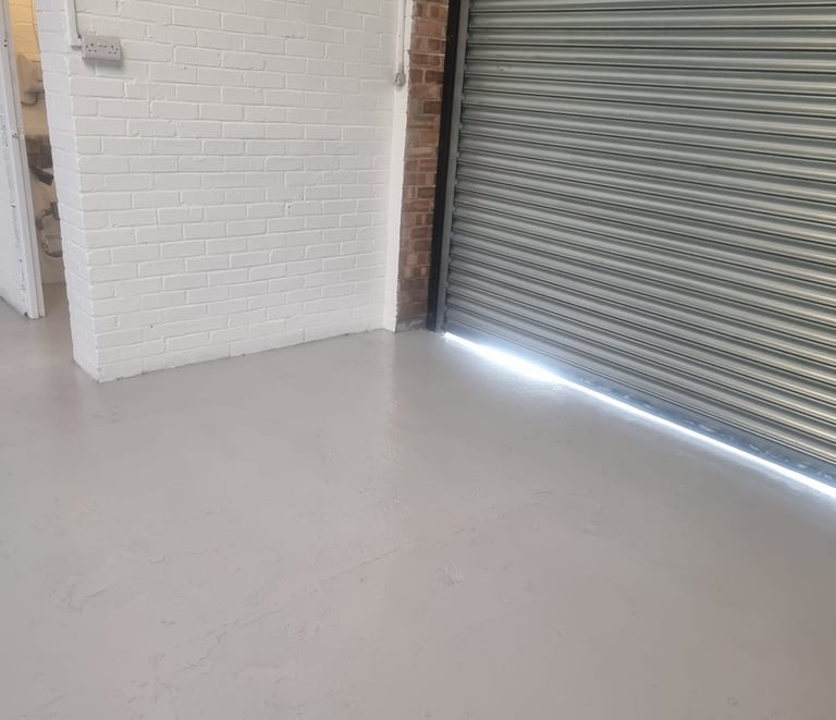 A corner of an industrial unit, with painted white brick walls, grey floor, and metal shutter door.