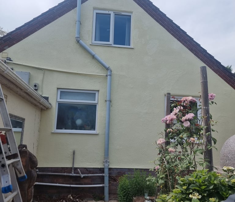 Exterior of a large house, with cream-painted walls, white window frames, and unpainted brick base.