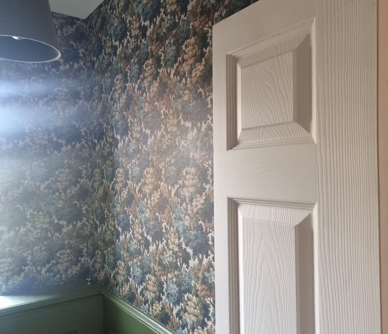 A room with forest-like wallpaper, green-painted wooden panels underneath, and a cream door.