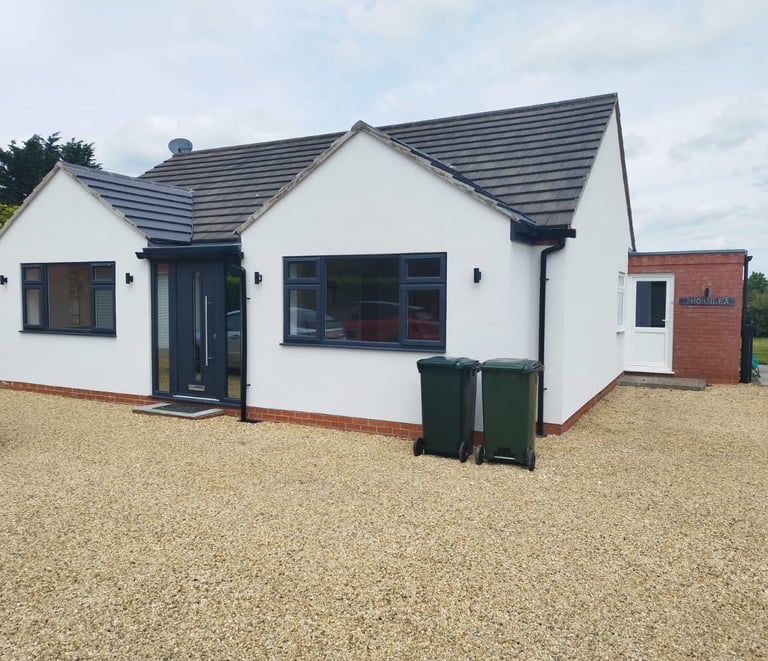 Exterior of a painted-white bungalow, with a black-tiled roof and black detailing.