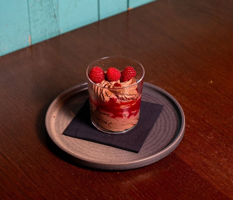 Schokolmbeer-Faden-Soufflé im Glas mit Hiruchtpüree und frischen Himbeeren, serviert auf einem runde