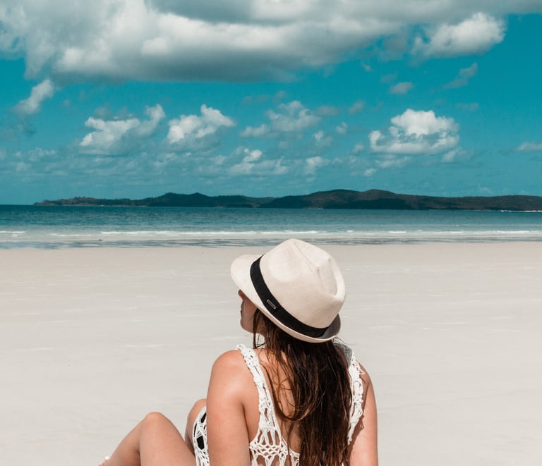 a woman sitting on a beach with a hat on