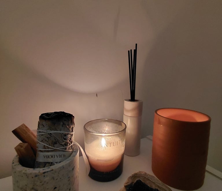 A spiritual wellness set featuring a lit scented candle, white sage smudge stick, and palo santo.