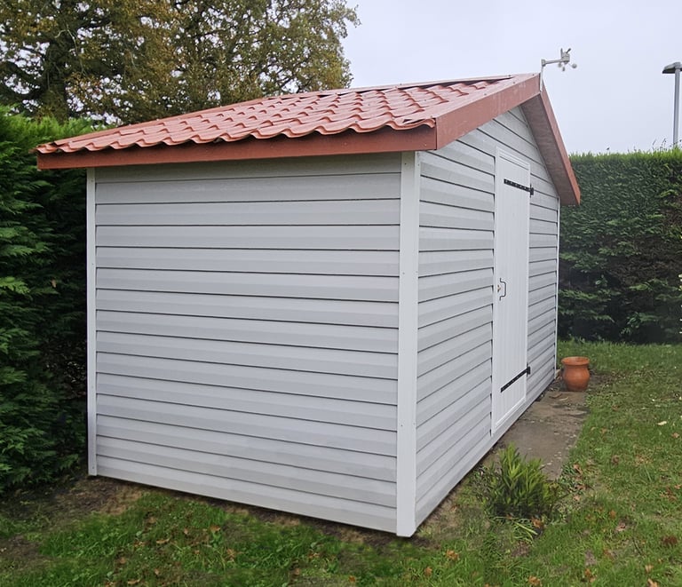 abri de jardin avec bardage vynil, toit en bac acier imitation tuile et débord de toit périphérique.