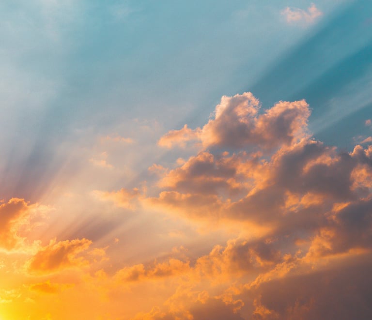 Golden sunbeams piercing through orange sunset clouds in a vibrant blue sky.
