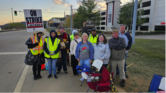 Large group of people standing with a on strike sign