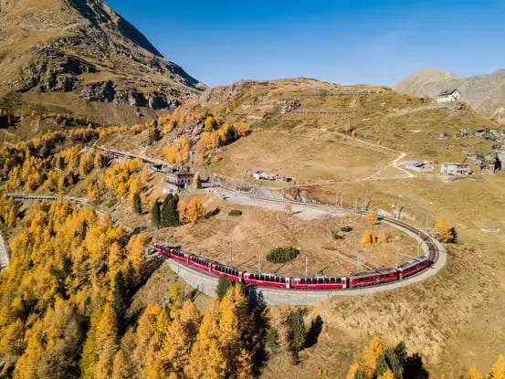 Scenic train ride on a curved track in the Swiss mountains during autumn.