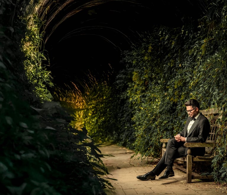 Groom sitting on a wooden bench in a vine-covered tunnel, captured by Fred Art Studio.