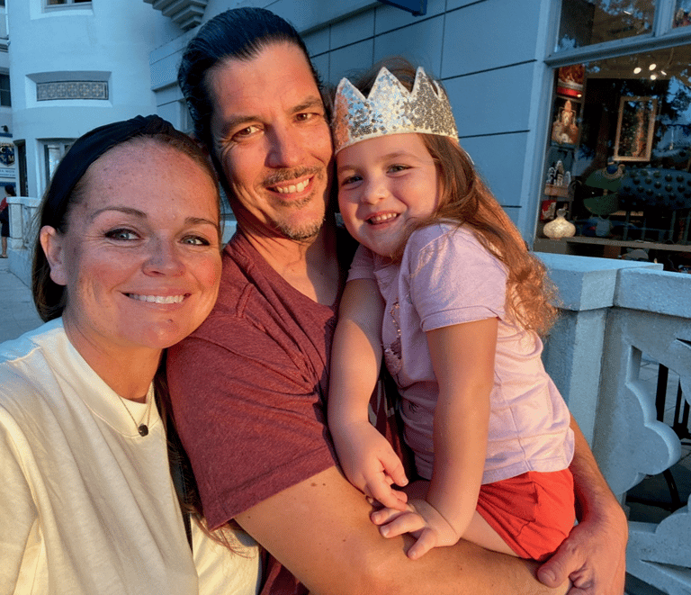 Smiling family selfie with daughter wearing a gold glitter crown