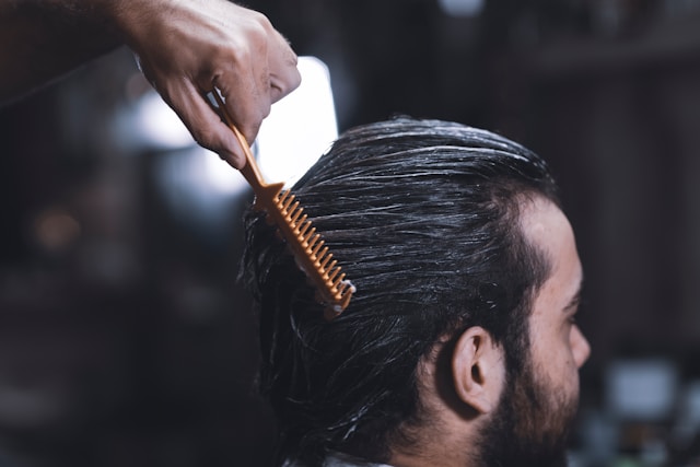 Coiffeur peignant les cheveux mouillés d’un homme vers l’arrière.