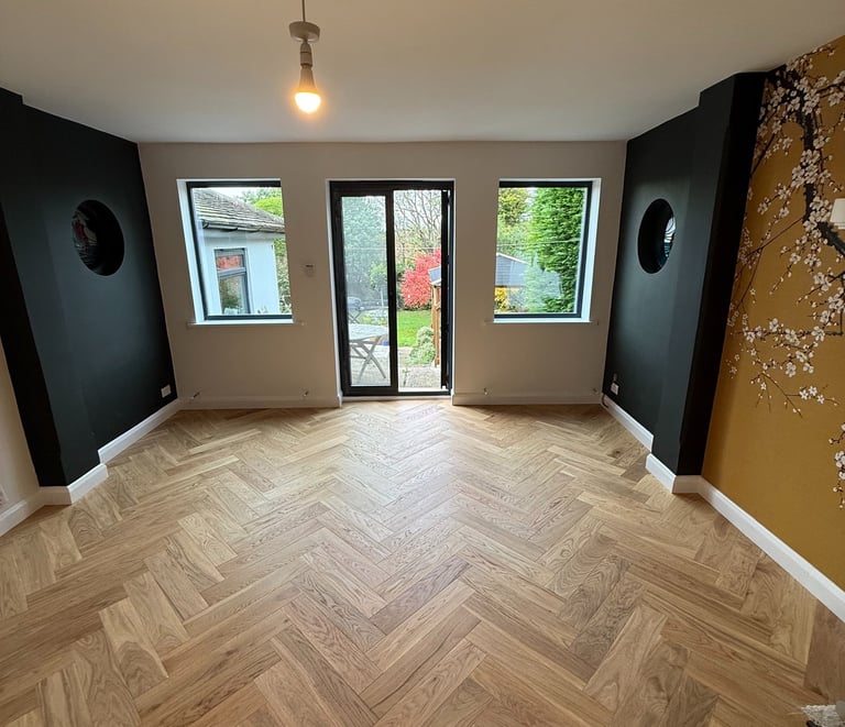 Modern living room with herringbone oak wood flooring, black accent walls, and floral mural in Hove.