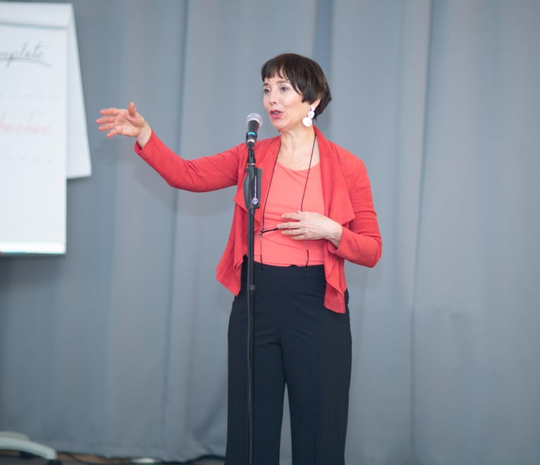 Female public speaking coach, wearing red vest, talking behind microphone, explain with hand gesture