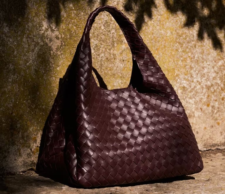 Bottega Veneta Luxury woven leather handbag in deep brown displayed outdoors.