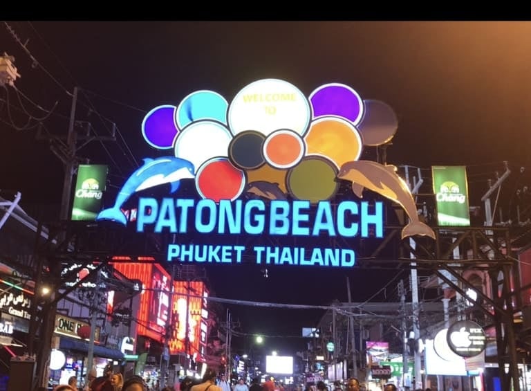 Beleuchtetes Neonschild von Patong Beach in Phuket, mit bunten Lichtern und Delfin-Figuren bei Nacht