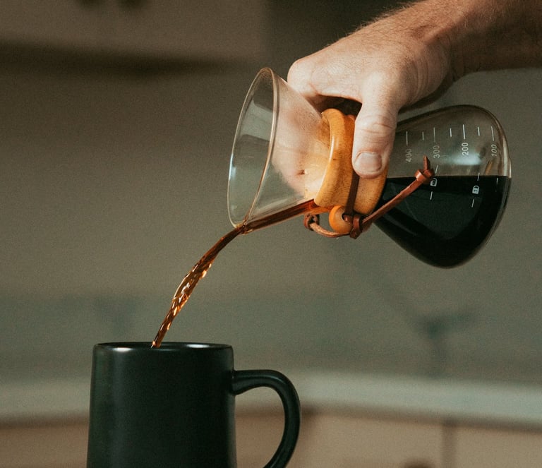 Mano sirviendo café filtrado en una taza negra usando chemex, mostrando métodos de preparación artes