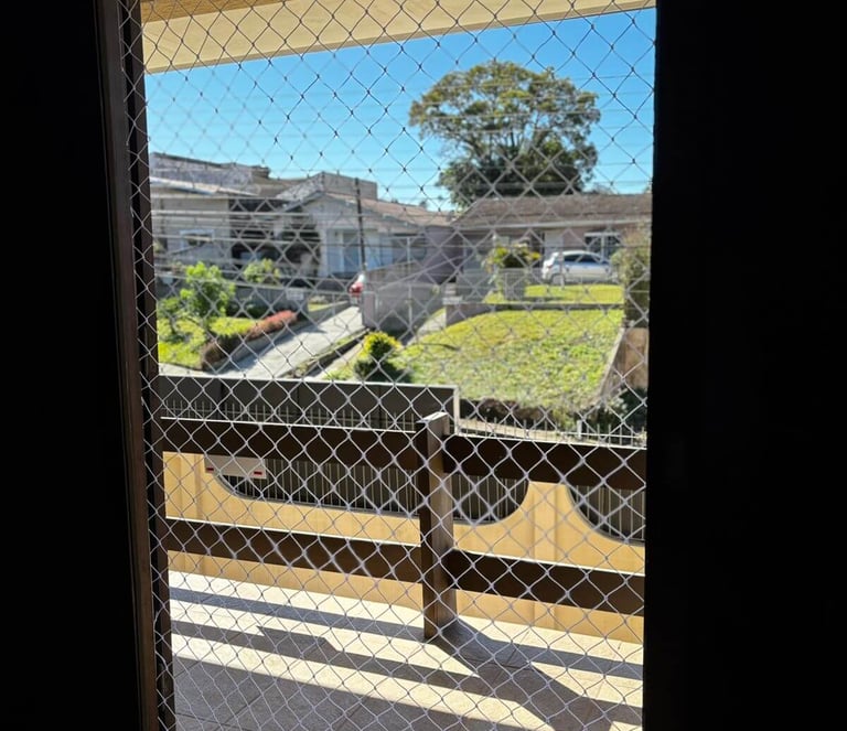Porta da sacada vista por dentro com rede de proteção instalada.