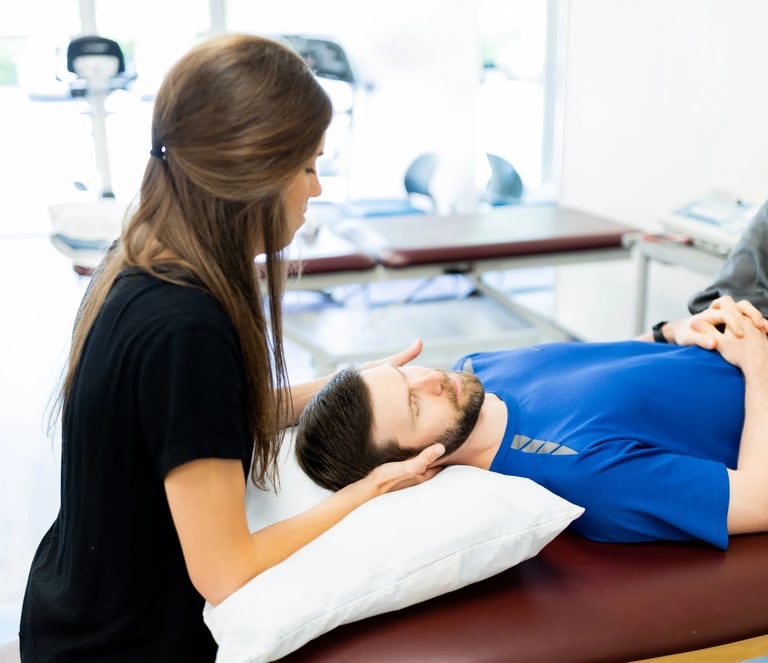 A female physical therapist providing neck manual therapy to a male patient in a clinic.