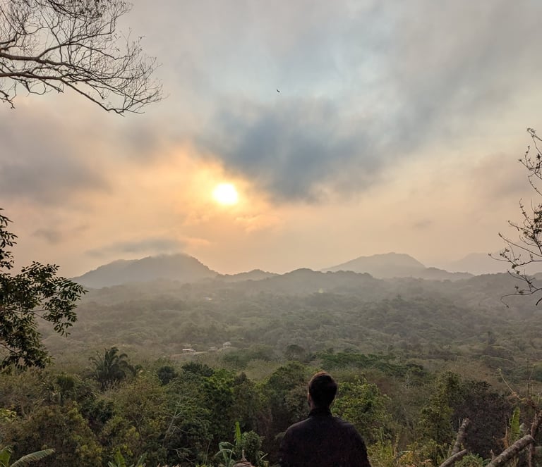 A hiker looking at a scenic mountain sunrise over a lush tropical jungle valley.
