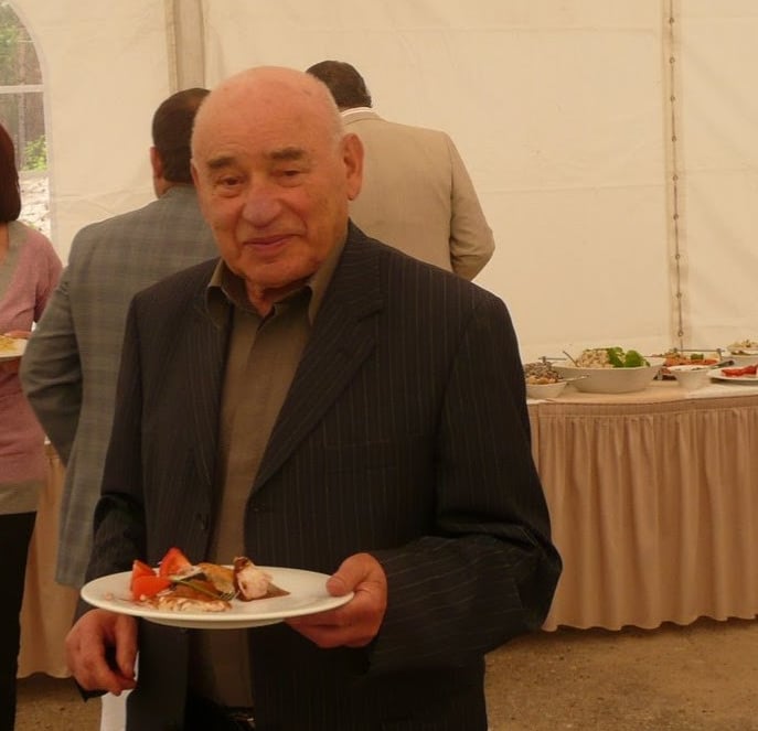 An elderly man in a pinstripe suit holding a plate of food at a catered buffet event.