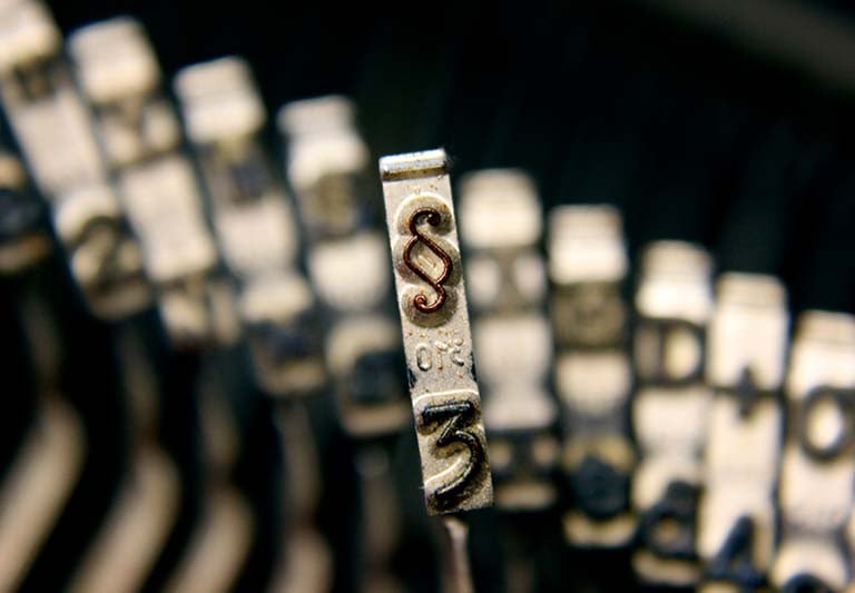 Close-up of a vintage typewriter key showing the section symbol, representing legal writing and law.