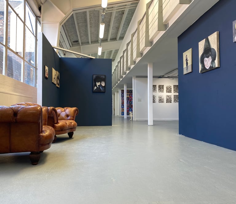 Oil Paintings hung on dark blue walls in a large gallery. There is a window and seating to the left.