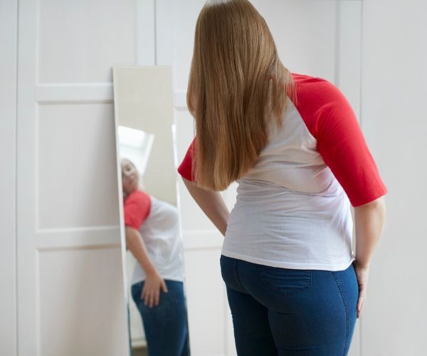 a woman in jeans and a red shirt is standing in front of a mirror