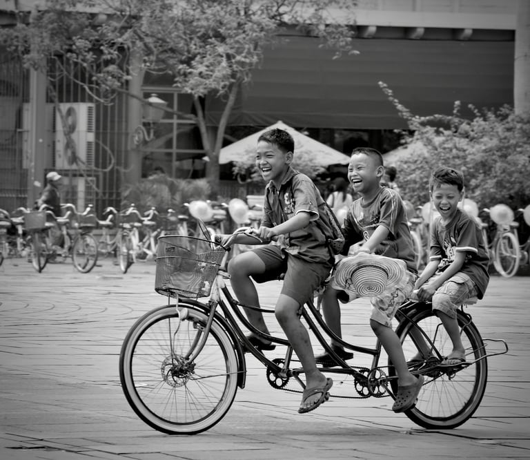 Three joyous youngs Indonesian boys on a bicycle riding in the main square of Kota Tua, Jakarta