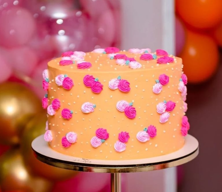 Bolo decorado com rosas coloridas em um suporte dourado, rodeado por balões em tons vibrantes. Ideal
