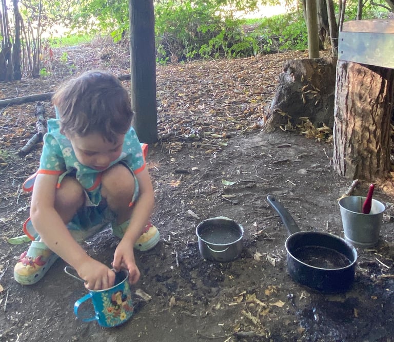 a young child in a woodland playing with a mud kitchen