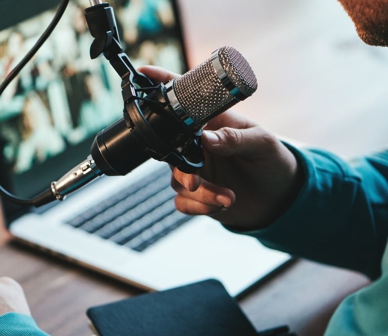 A person recording a podcast using a professional condenser microphone and a laptop computer.