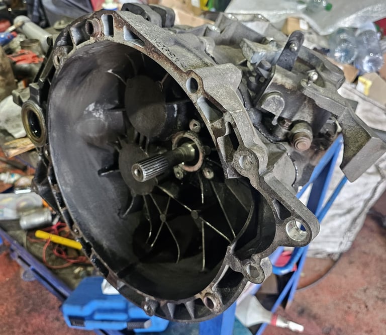 A used manual transmission gearbox housing on a blue stand in an automotive repair shop.