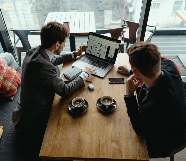 Two businessmen in a cafe discussing data analytics on a laptop over coffee.