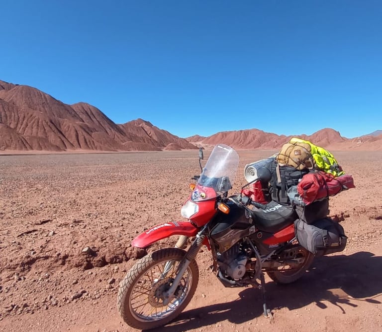 a motorcycle parked in the desert with a backpack on it cono de arita puna atacama salar