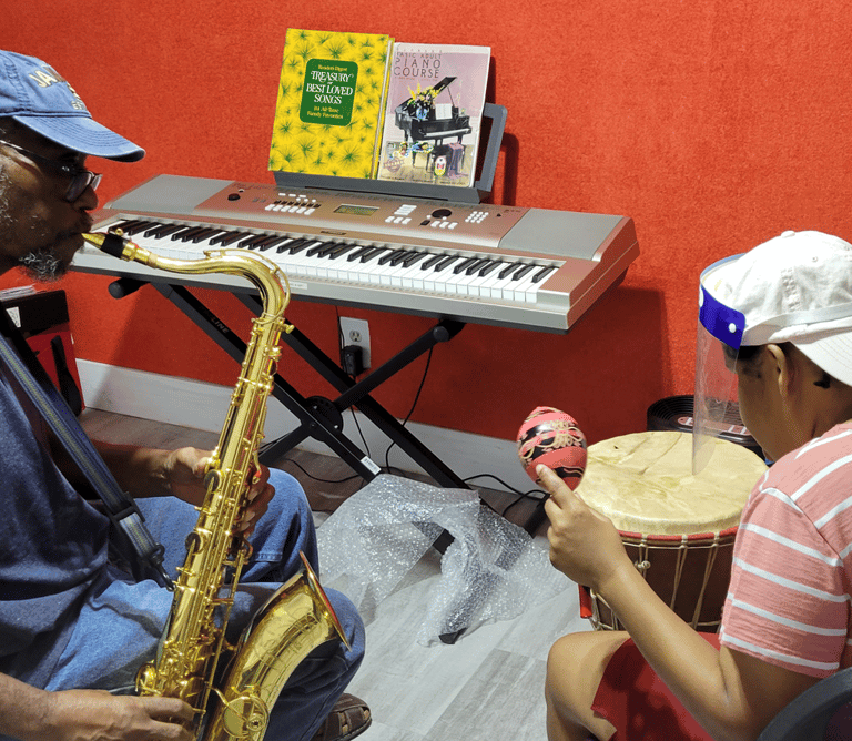 a man playing a saxophone and a woman playing playing a drum and shaking a maraca