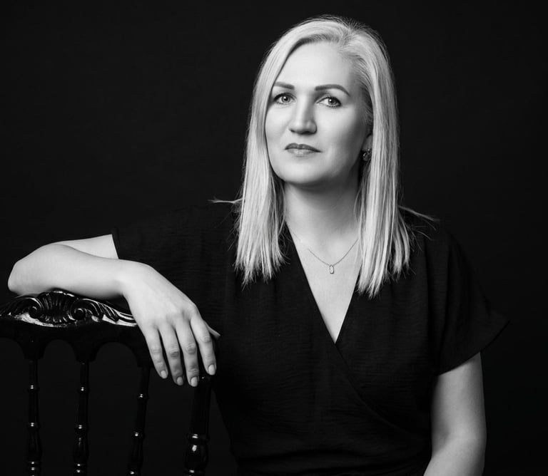 Black and white professional headshot of a blonde woman leaning on a chair against a dark background.