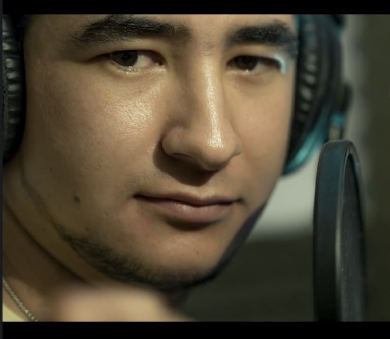 Un cantante masculino con audífonos profesionales grabando frente a un micrófono de estudio.